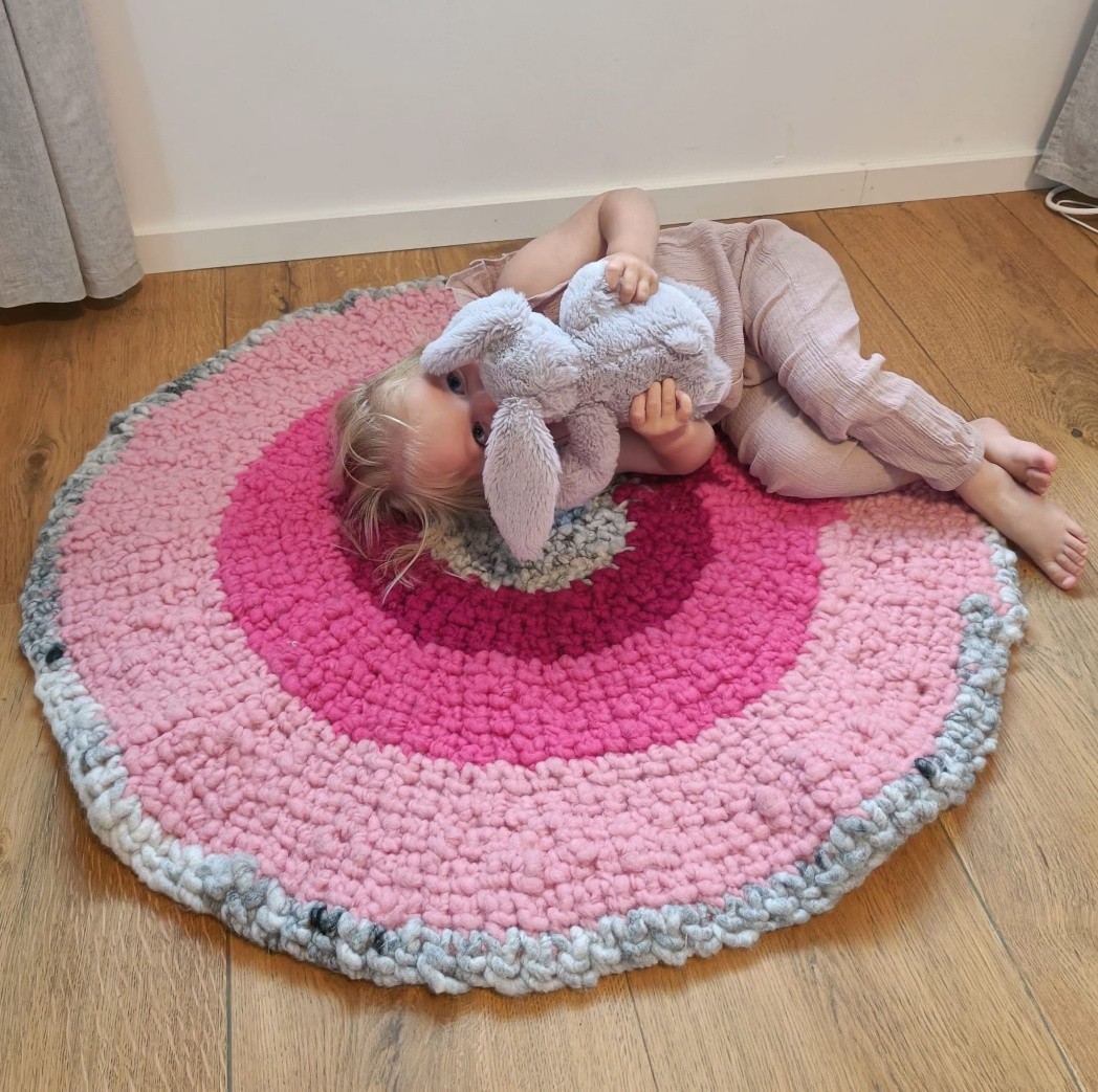 Kind liegt auf einem runden rosa Teppich und hält ein Stofftier
